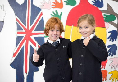 Two primary aged children smiling, giving thumbs up with a decorative background with international flags.